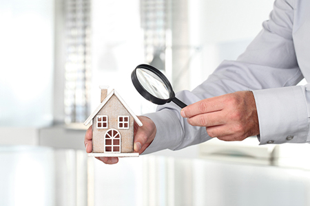 Man holding a house model under a magnifying glass, symbolizing differences in home inspector credentials in Missouri vs. Illinois